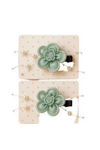 Two green succulent-shaped hair clips on a white card with a beige background