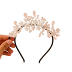 Decorative headband with floral and bead details held by a hand on a white background