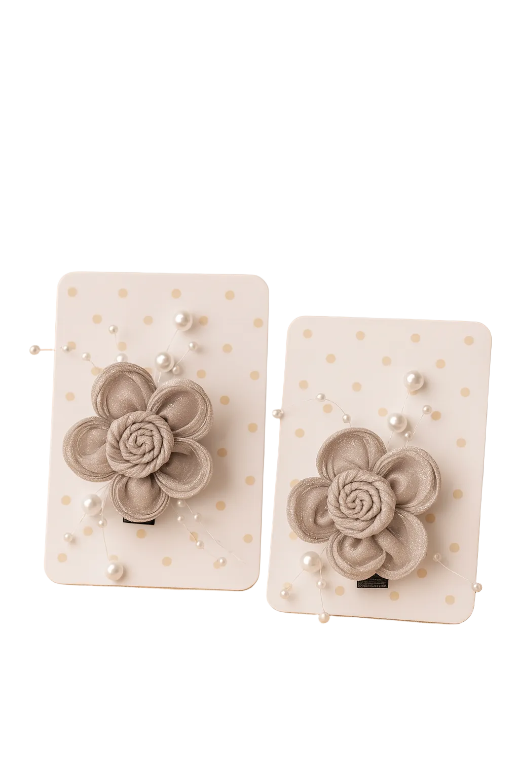 Pair of beige flower-shaped earrings on white cards with gold polka dots, placed on a beige surface with a plant in the background.