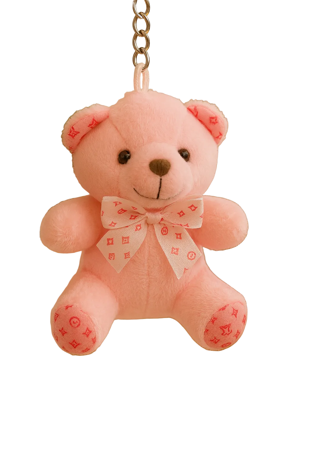 Pink teddy bear keychain with a bow tie against a blurred indoor background