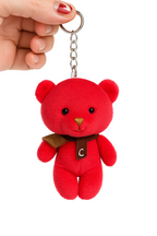 Red teddy bear keychain held by a hand on a white background