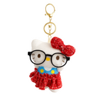 White cat-shaped keychain with red bow, glasses, and blue dress on a white background