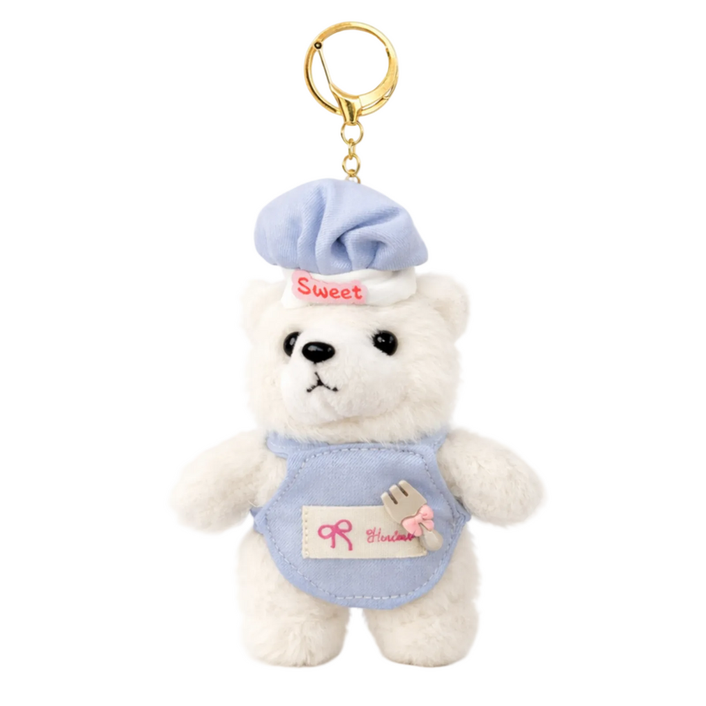 Small white teddy bear keychain with a blue outfit and hat on a white background